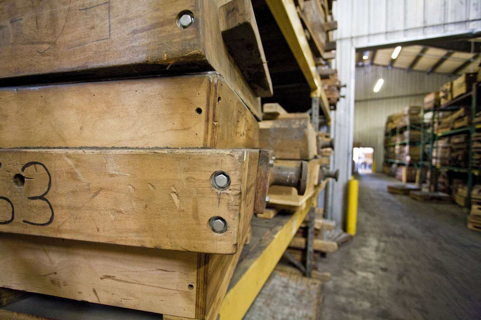 In a spacious, well-lit warehouse of CL Dews & Sons Foundry, a close-up reveals large wooden molds stacked on metal shelves. Bearing numbers and secured with bolts, these molds hint at the rich history of the green sand molding process that shaped Carrington Luther Dews Sr.'s legacy.