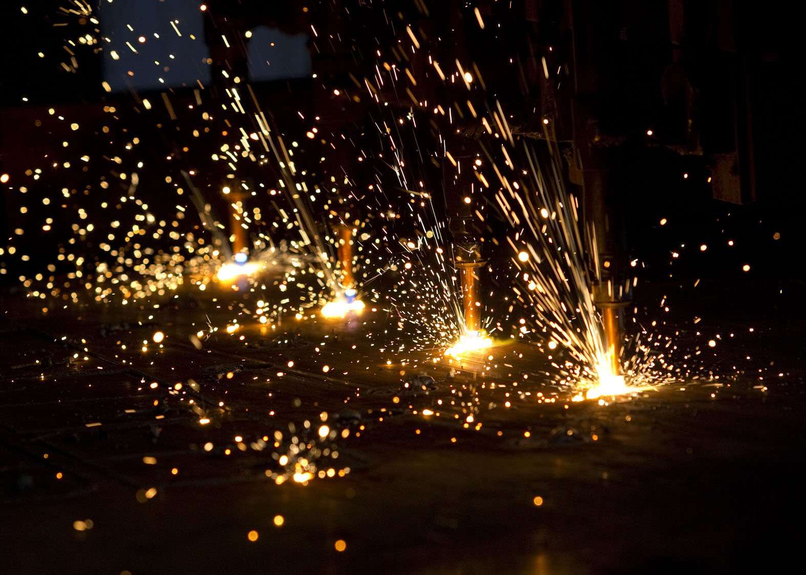 Bright sparks and glowing embers fly from welding torches against a dark background, mirroring the fiery legacy of CL Dews & Sons Foundry. The dynamic scene echoes a history of innovation and craftsmanship.